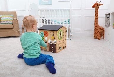 Cute little boy playing with busy board house on floor at home