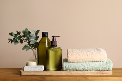 Photo of Solid shampoo bar and bottles of cosmetic product on wooden table near beige wall