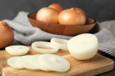 Wooden board with cut onion and bowl of bulbs on table