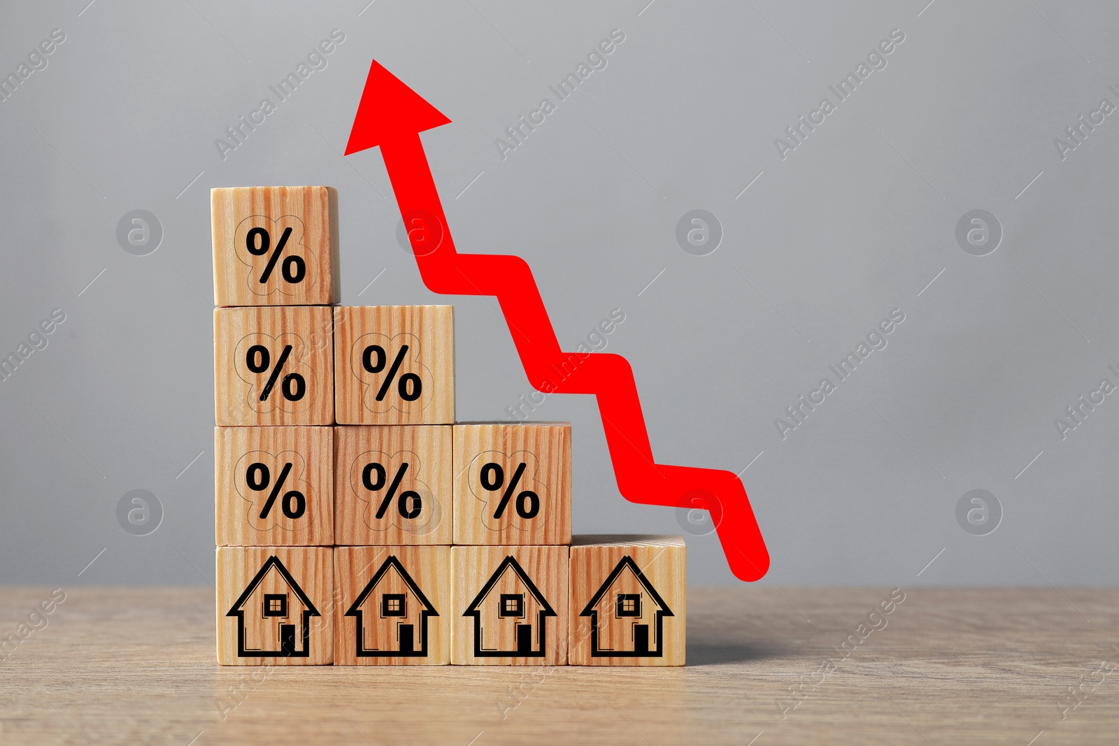Image of Mortgage rate rising illustrated by upward arrow over cubes with percent signs and house icons on wooden table