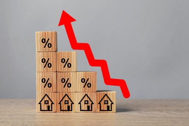 Mortgage rate rising illustrated by upward arrow over cubes with percent signs and house icons on wooden table