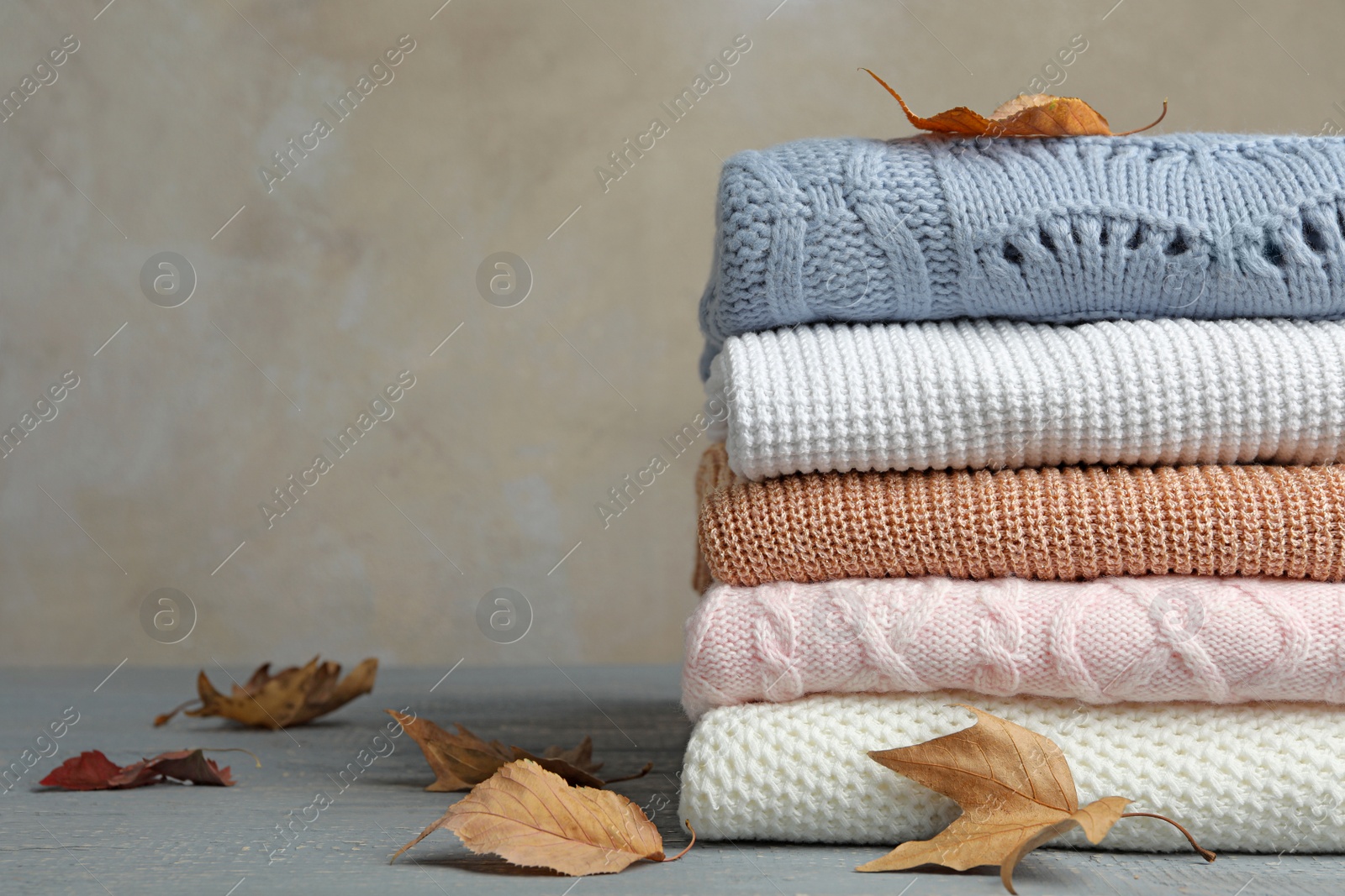 Photo of Stack of warm clothes and autumn leaves on wooden table against grey background. Space for text