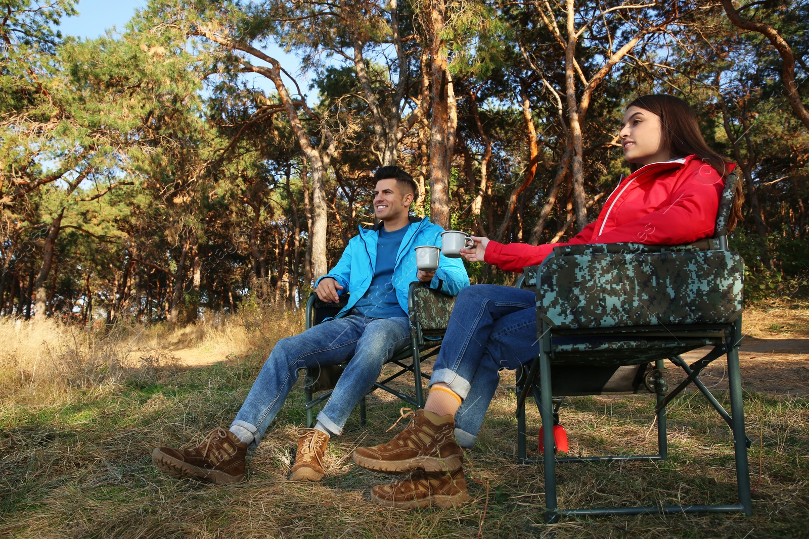 Photo of Couple resting in camping chairs and enjoying hot drink outdoors