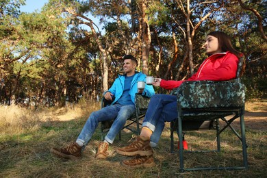 Couple resting in camping chairs and enjoying hot drink outdoors