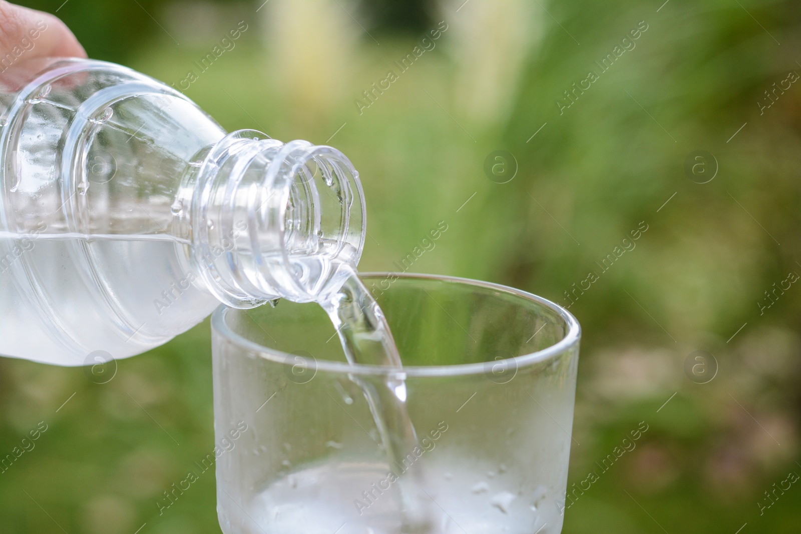 Photo of Woman pouring water from bottle into glass outdoors, closeup