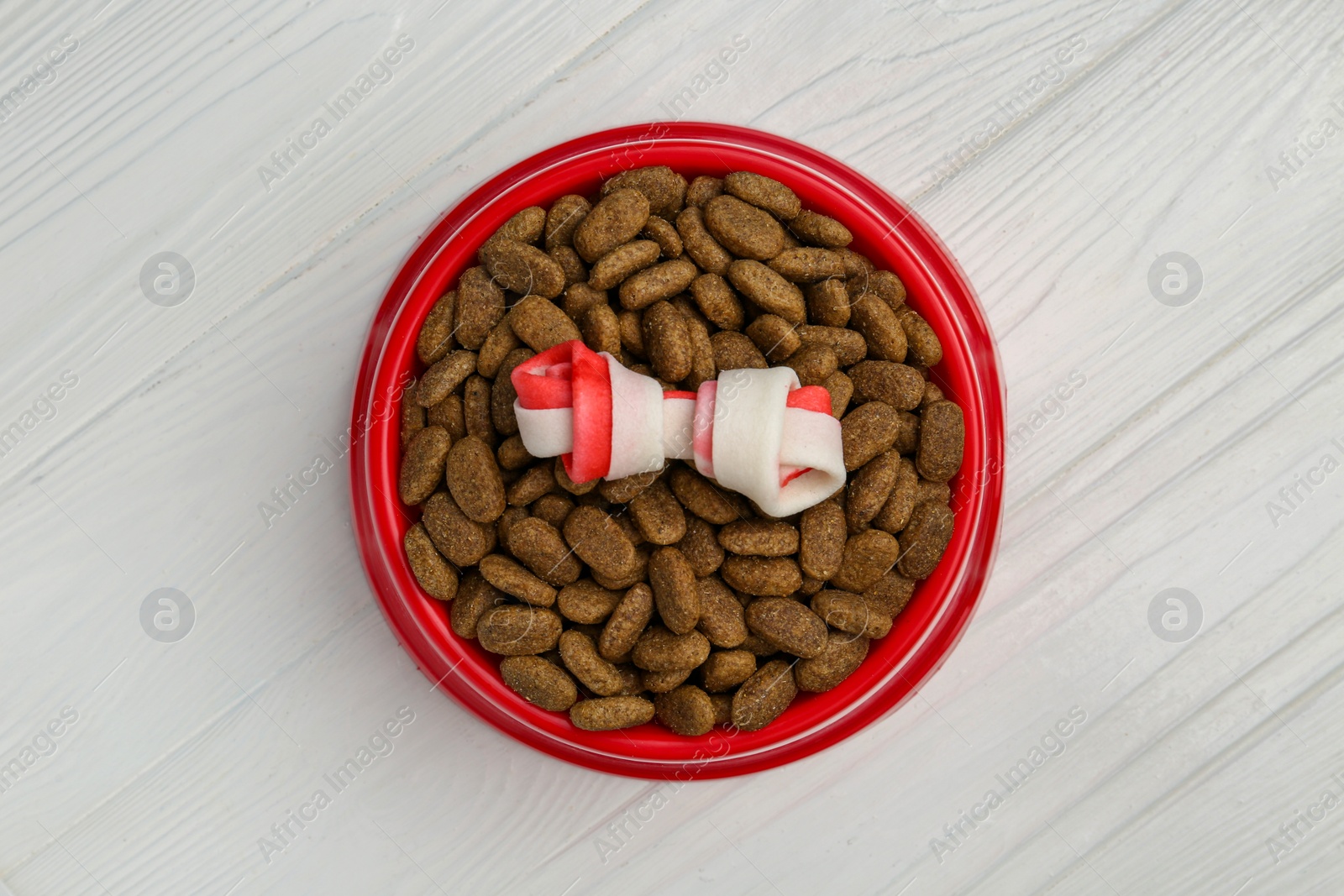 Photo of Dry dog food and treat (knotted chew bone) on white wooden floor, top view