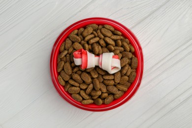 Dry dog food and treat (knotted chew bone) on white wooden floor, top view