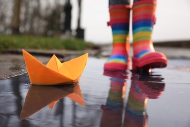 Photo of Little girl outdoors, focus on paper boat in puddle