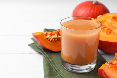 Photo of Tasty pumpkin juice in glass, whole and cut pumpkins on white wooden table. Space for text