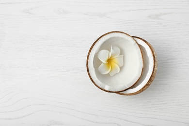 Photo of Halves of coconut and flower on white wooden background, top view. Space for text