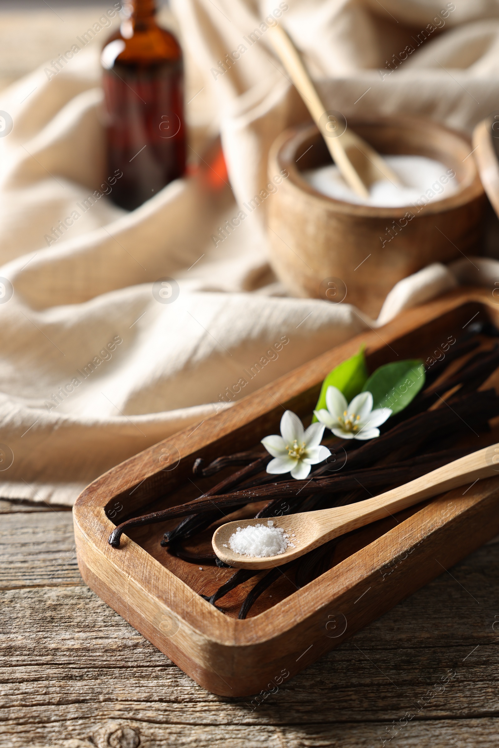 Photo of Vanilla pods, flowers, leaves and spoon with sugar on wooden table, closeup