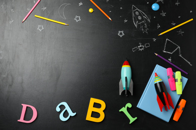 Bright toy rockets, school supplies and drawings on chalkboard, flat lay. Space for text