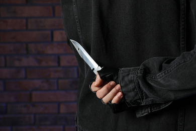 Photo of Man with knife behind his back near brick wall, closeup. Dangerous criminal