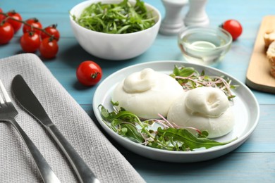 Photo of Delicious burrata cheese with arugula and microgreens served on light blue wooden table