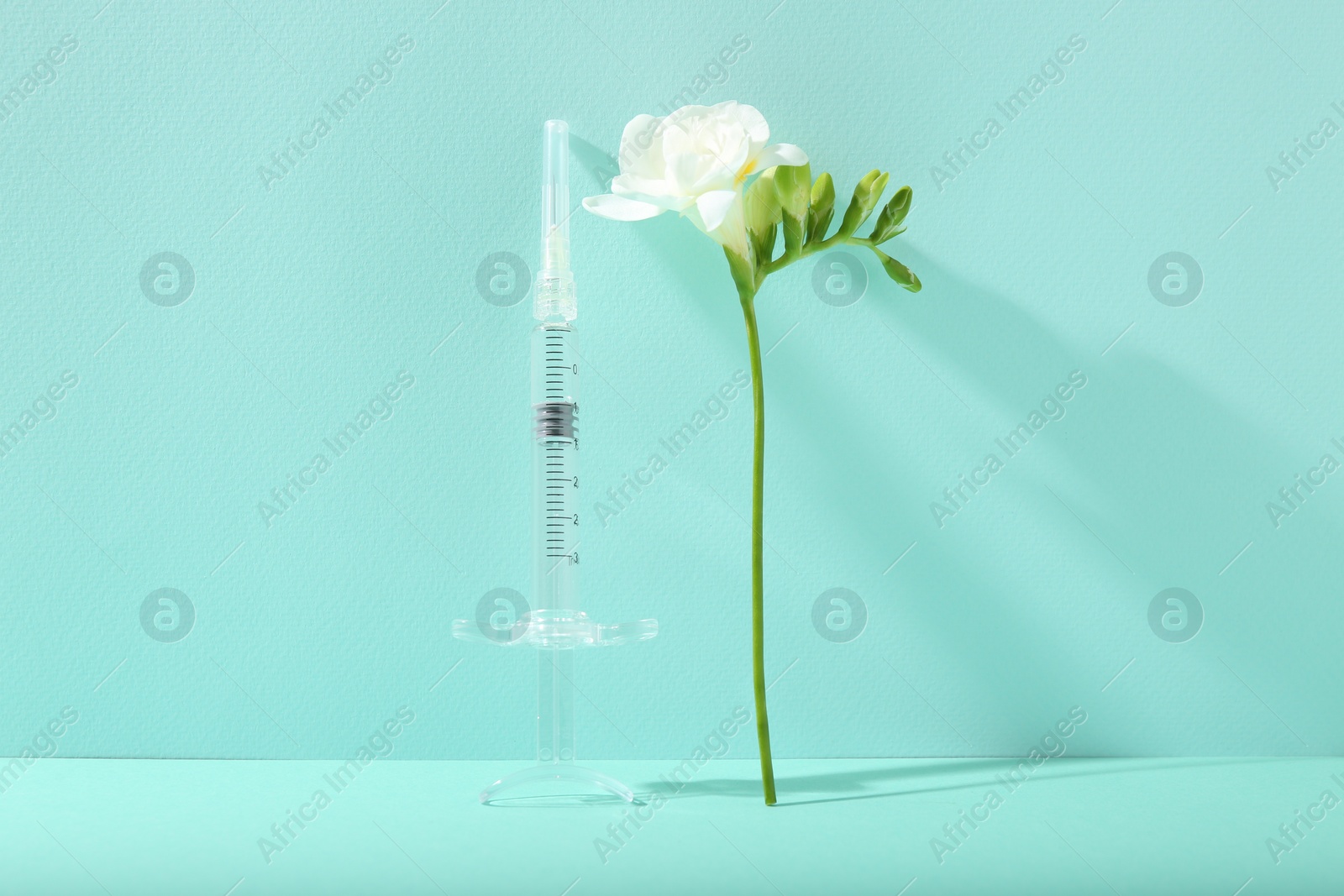 Photo of Cosmetology. Medical syringe and freesia flower on turquoise background