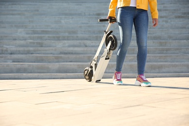 Photo of Woman carrying folded electric kick scooter outdoors. Space for text