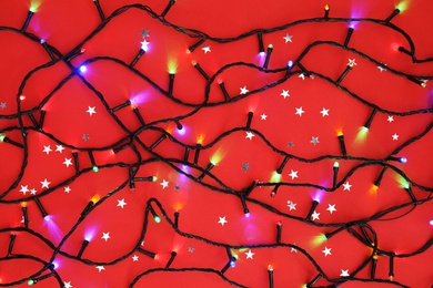 Glowing Christmas lights on color background, top view