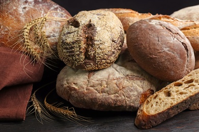 Photo of Different kinds of fresh bread on black wooden table, closeup