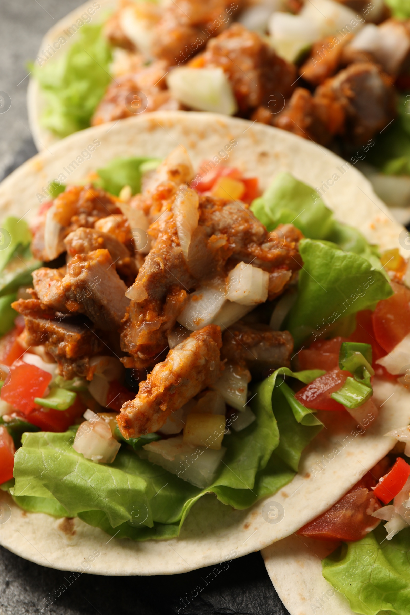 Photo of Delicious tacos with vegetables and meat on grey table, closeup