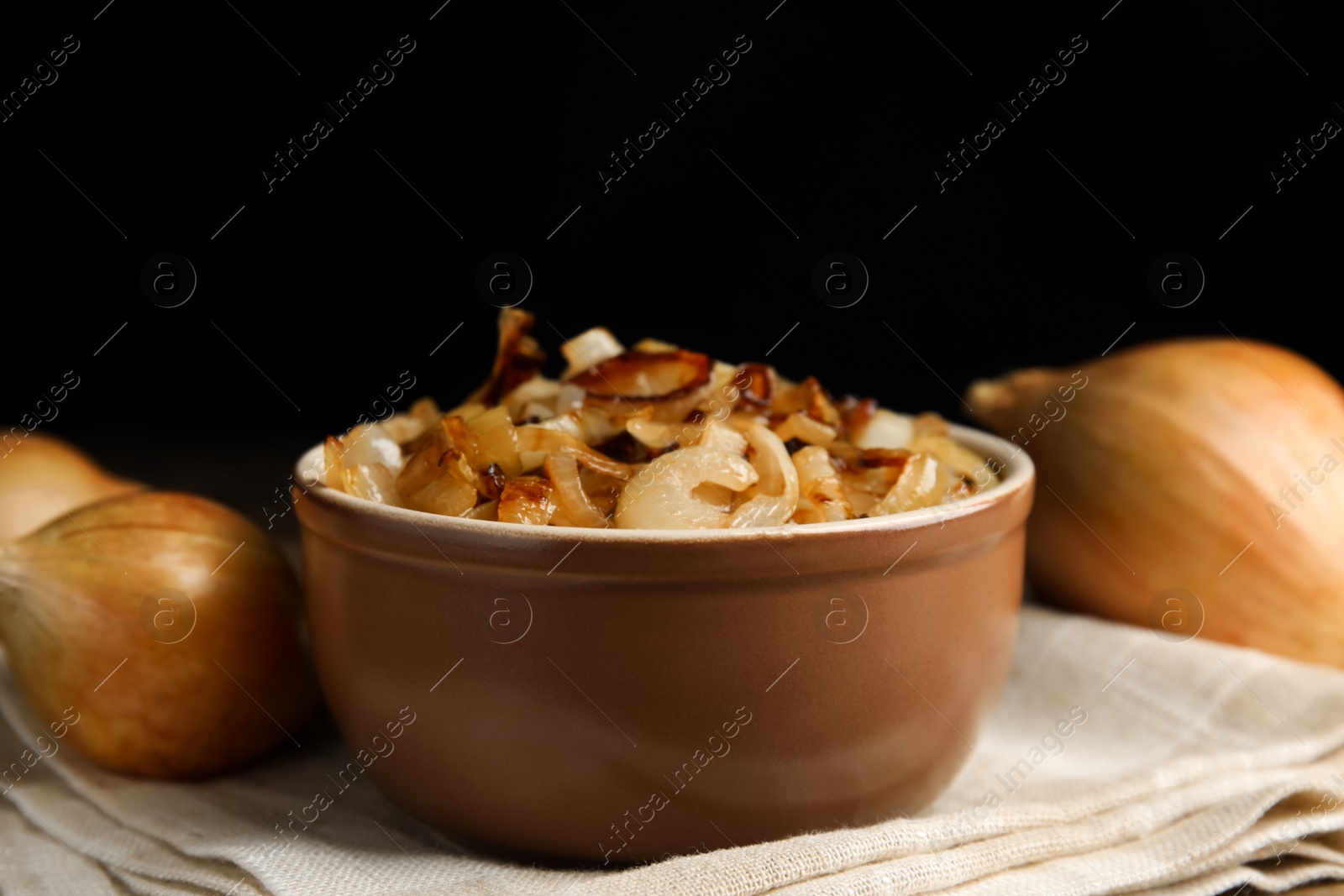 Photo of Tasty fried onion on napkin against black background
