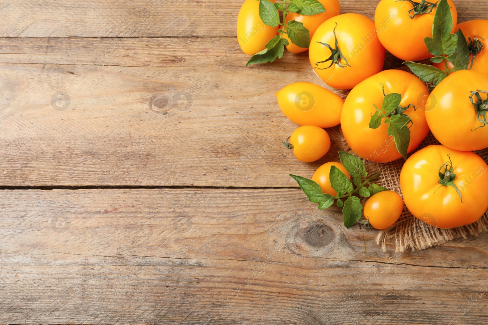 Photo of Fresh ripe yellow tomatoes with leaves on wooden table, flat lay. Space for text