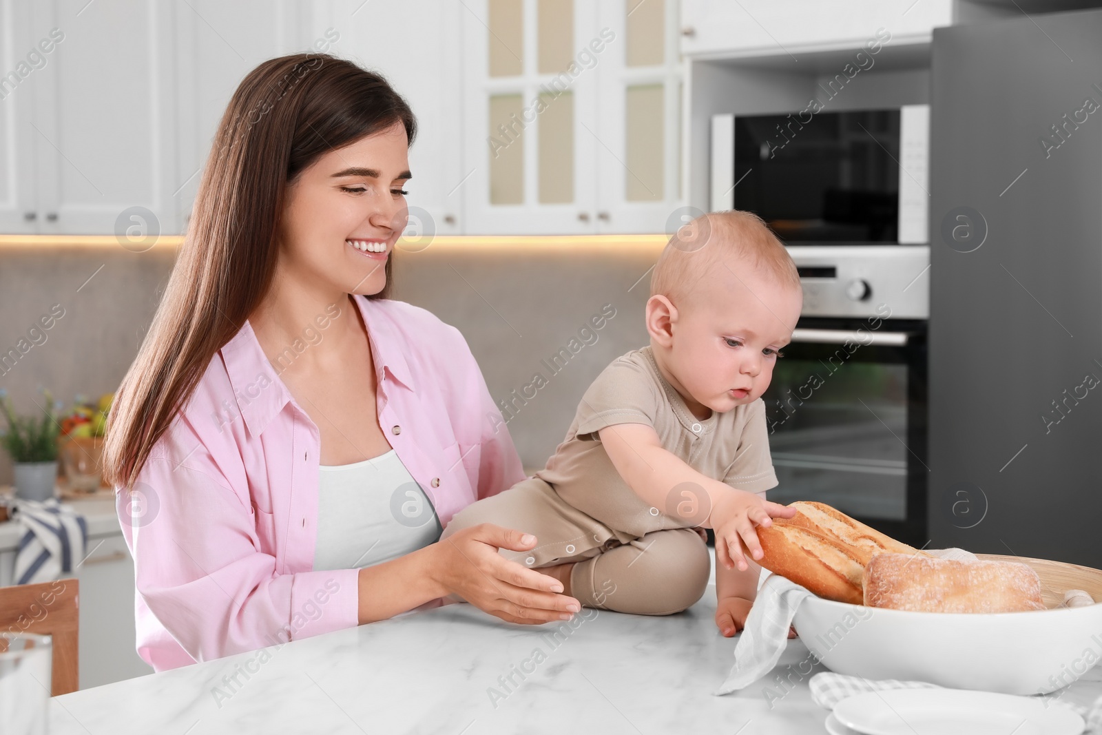 Photo of Happy young woman and her cute little baby spending time together in kitchen