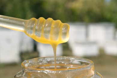 Photo of Taking delicious fresh honey with dipper from glass jar against blurred background, closeup