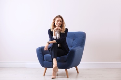 Beautiful young woman sitting in armchair indoors