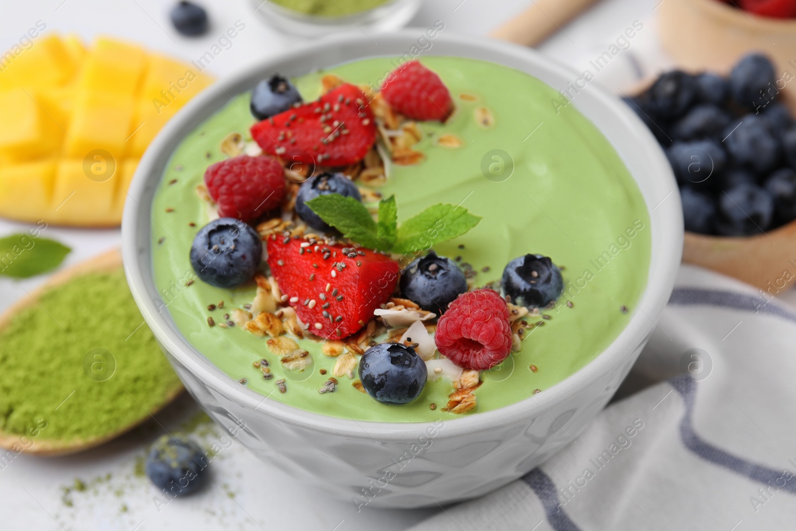 Photo of Tasty matcha smoothie bowl served with berries and oatmeal on white table, closeup. Healthy breakfast