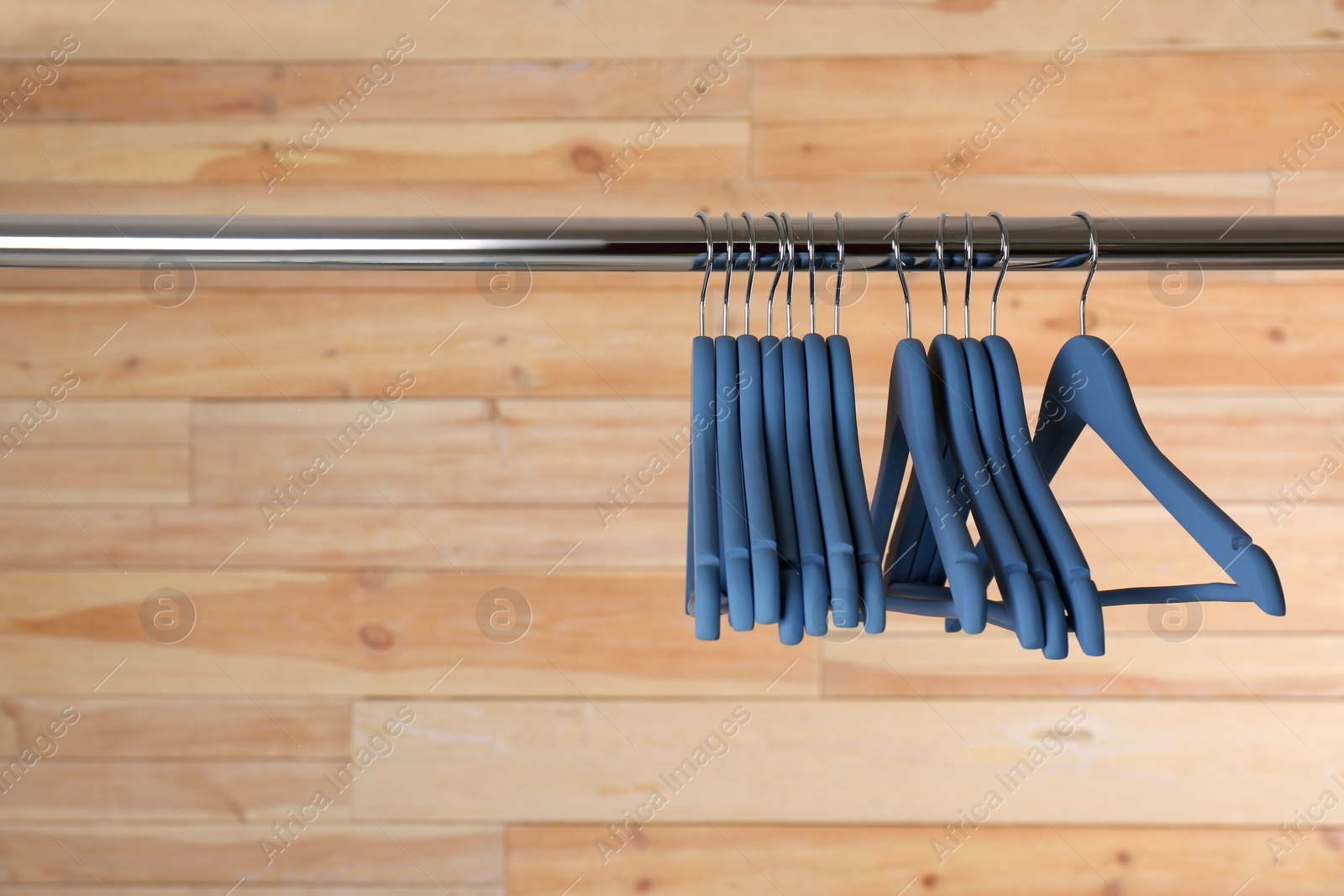 Photo of Metal rack with clothes hangers on wooden background, space for text