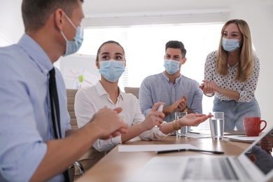 Coworkers with protective masks using hand sanitizer in office. Business meeting during COVID-19 pandemic