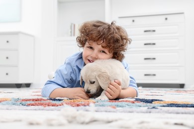 Photo of Little boy lying with cute puppy on carpet at home