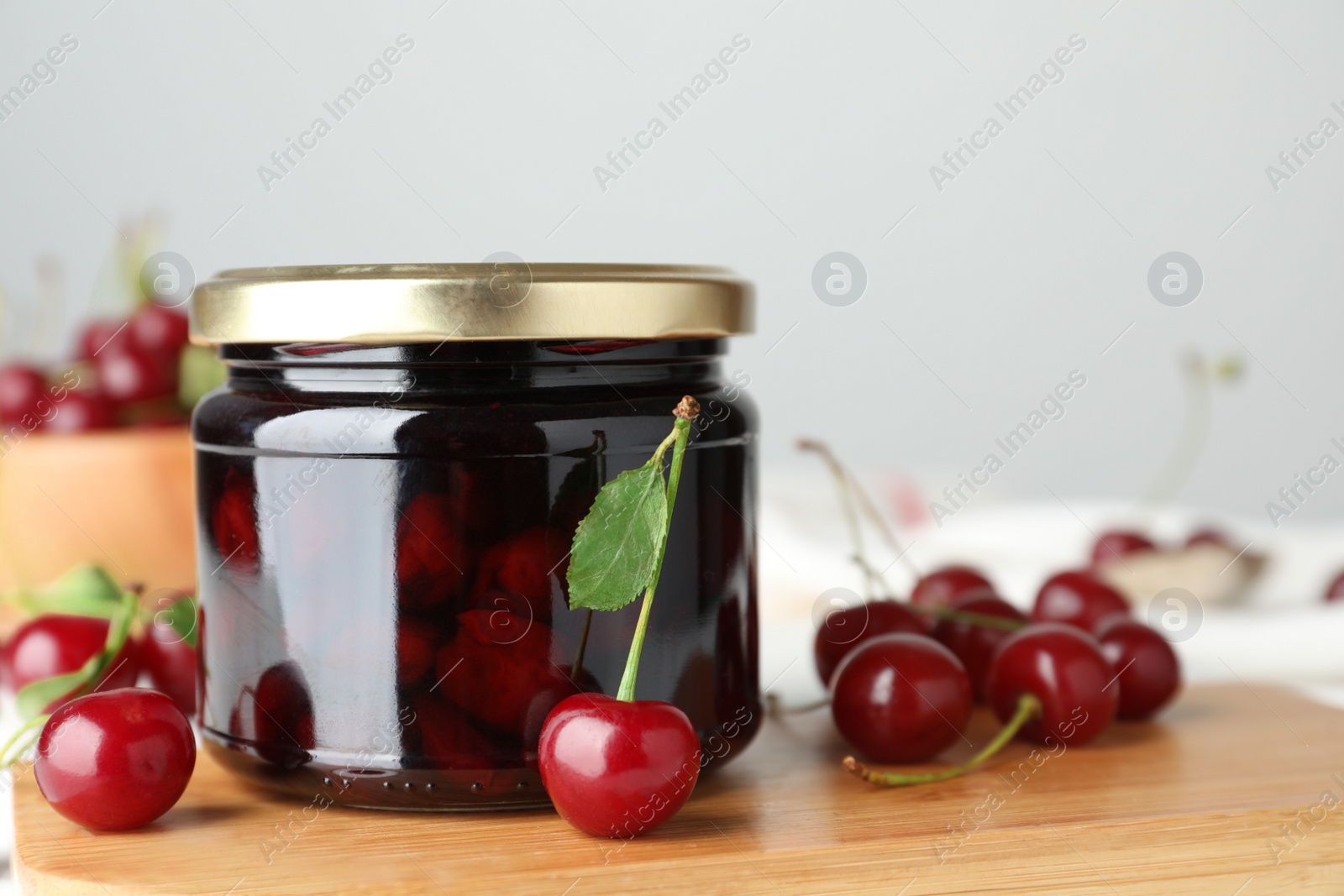 Photo of Jar of pickled cherries and fresh fruits on wooden board, closeup