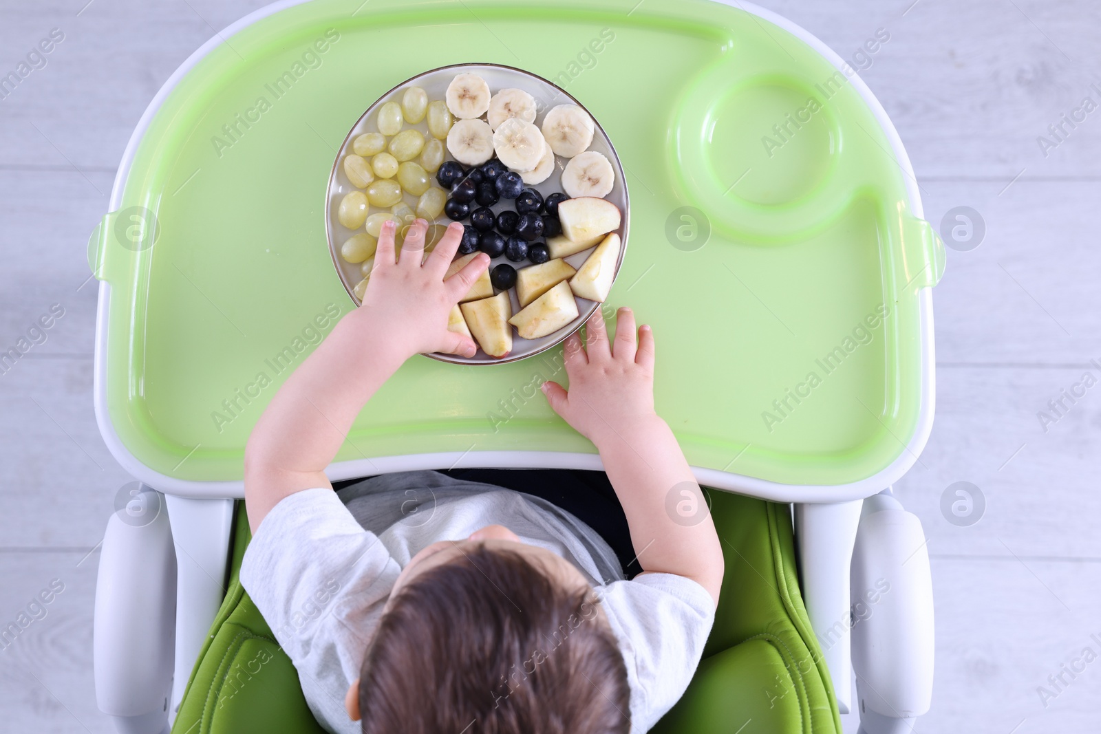 Photo of Cute little baby eating healthy food in high chair indoors, top view