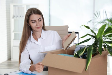 Happy young woman packing stuff in box at office