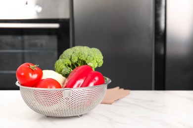 Photo of Colander with different fresh vegetables on white marble table in kitchen. Space for text