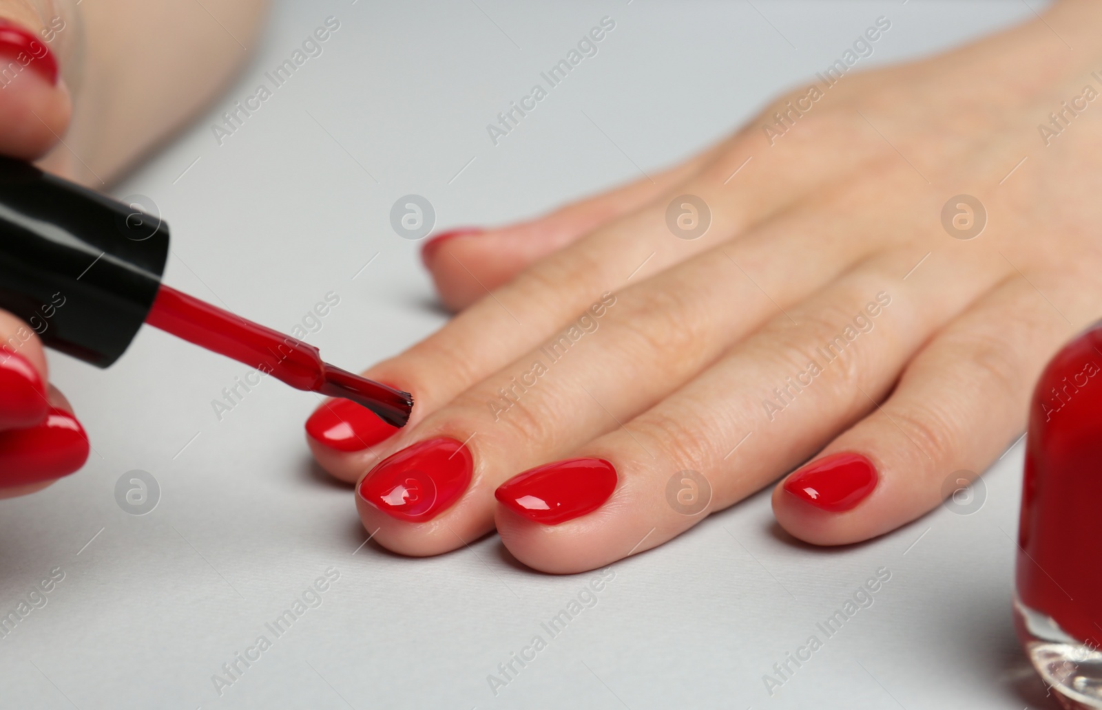 Photo of Woman painting nails with red polish on white background, closeup