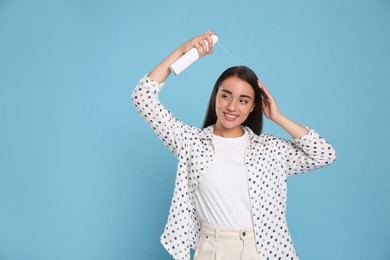 Photo of Young woman applying dry shampoo against light blue background