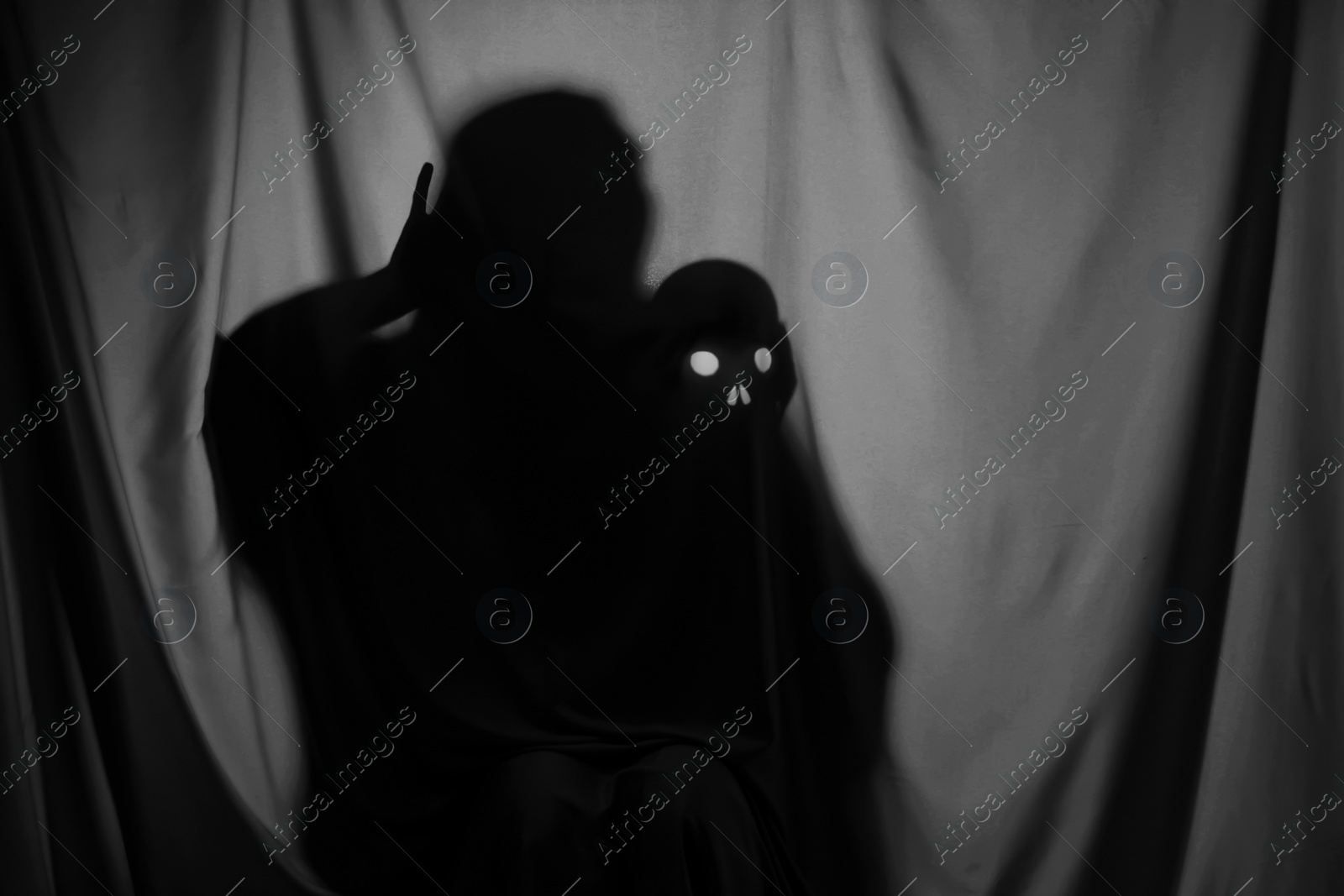 Photo of Silhouette of creepy ghost with skull behind grey cloth