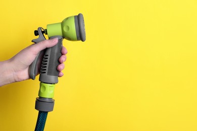 Photo of Woman holding watering hose with sprinkler on yellow background, closeup. Space for text