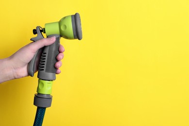 Woman holding watering hose with sprinkler on yellow background, closeup. Space for text