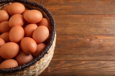 Photo of Raw chicken eggs in wicker basket on wooden table, space for text