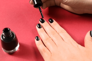 Woman applying black nail polish on color background, closeup