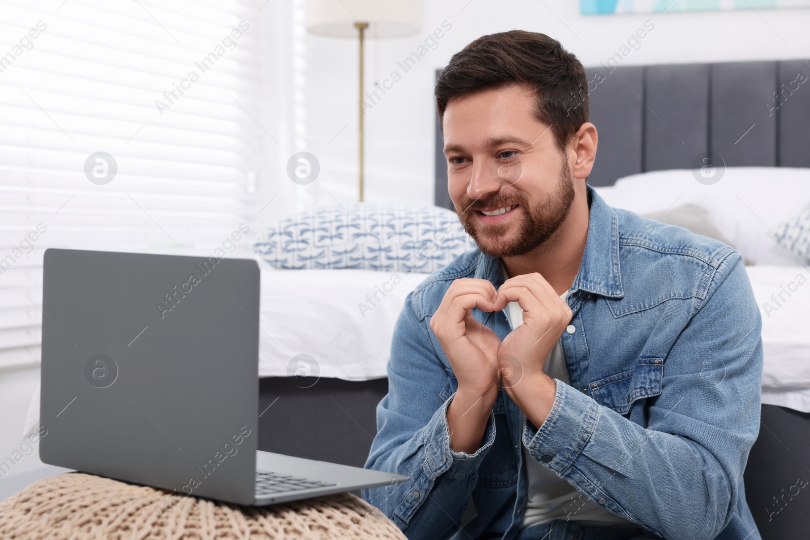 Photo of Happy man making heart with hands during video chat via laptop at home. Long-distance relationship