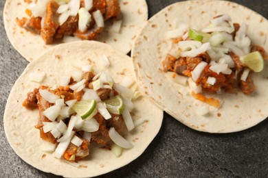 Photo of Delicious tacos with vegetables, meat and lime on grey textured table