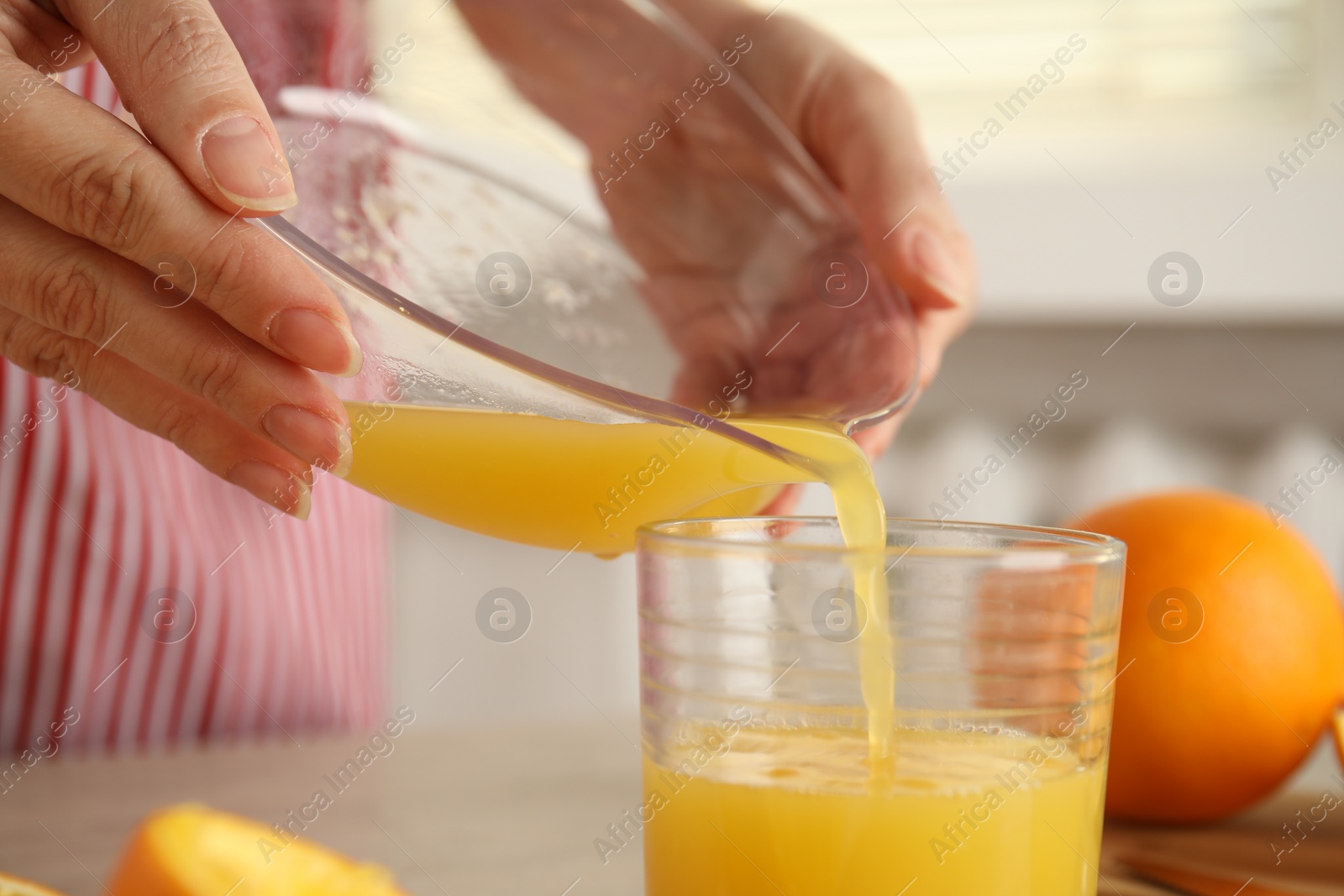 Photo of Woman pouring freshly made orange juice in glass at table, closeup