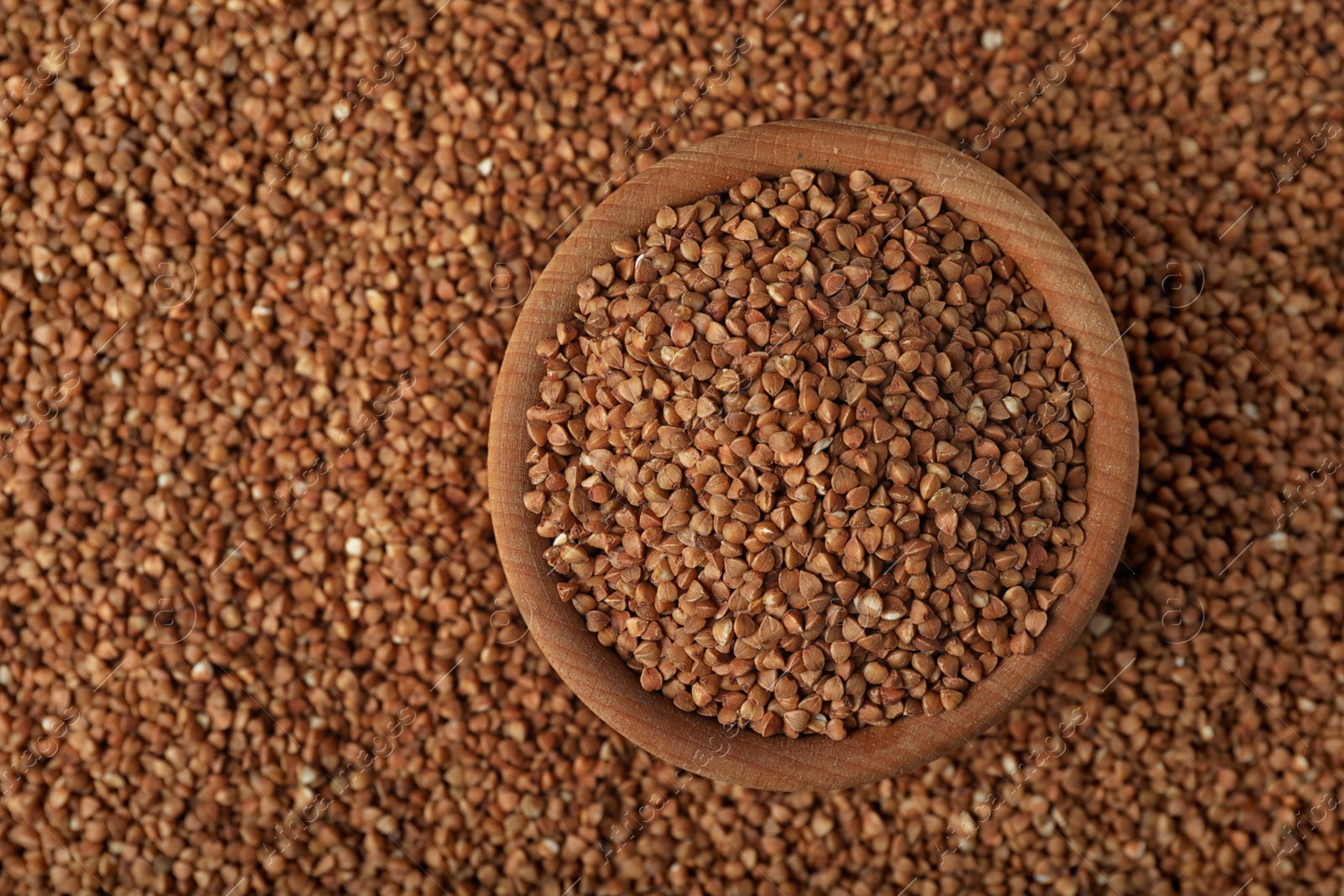 Photo of Uncooked buckwheat in bowl on grains, top view. Space for text