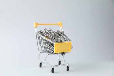 Photo of Metal nails in shopping cart on light grey background, closeup