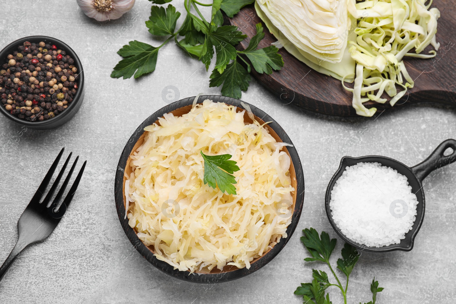 Photo of Bowl of tasty sauerkraut and ingredients on grey table, flat lay