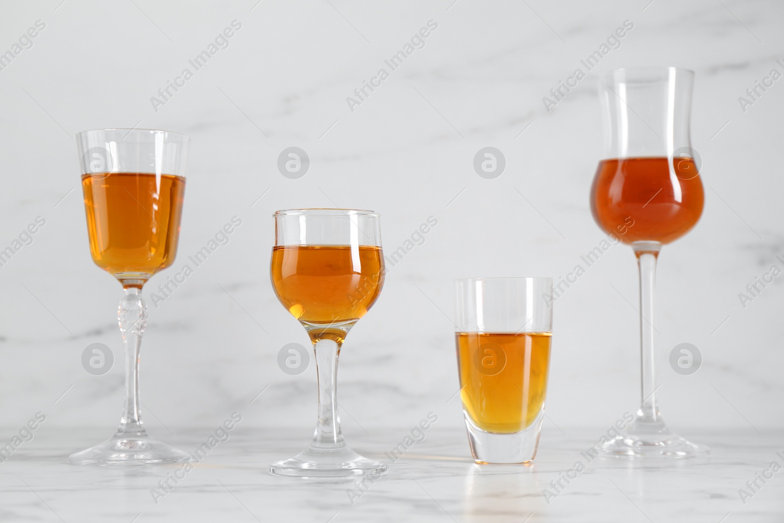 Photo of Different delicious liqueurs in glasses on white marble table